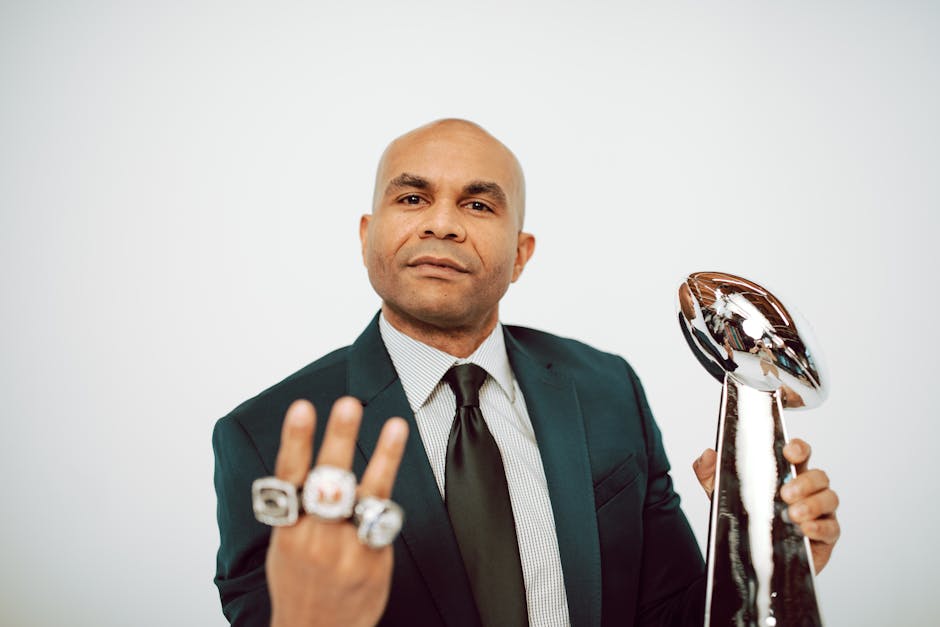 Confident man in a suit showcasing victory rings and trophy on a white background